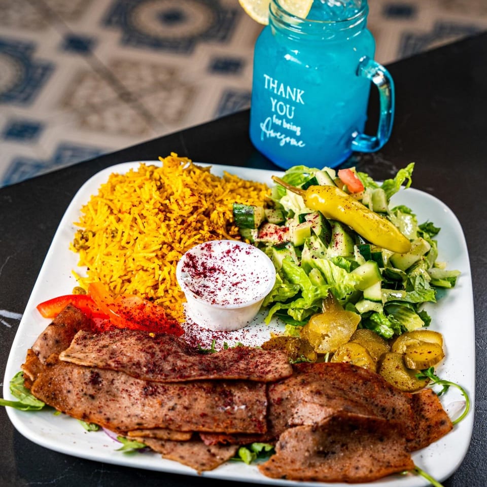 Hala Cafe's Mediterranean platter with gyro meat, yellow rice, salad, pickles, and a blue drink.