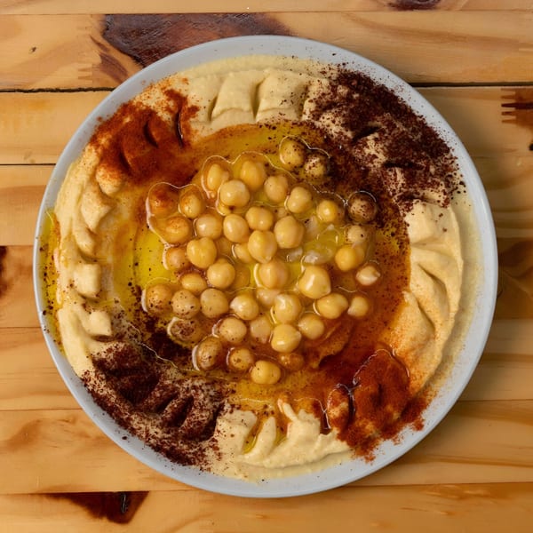 Hala Cafe's hummus, topped with chickpeas, olive oil, paprika, and sumac, on a wooden table.