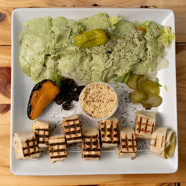 A Mediterranean platter with green salad, hummus, grilled wraps, olives, and pickled peppers.