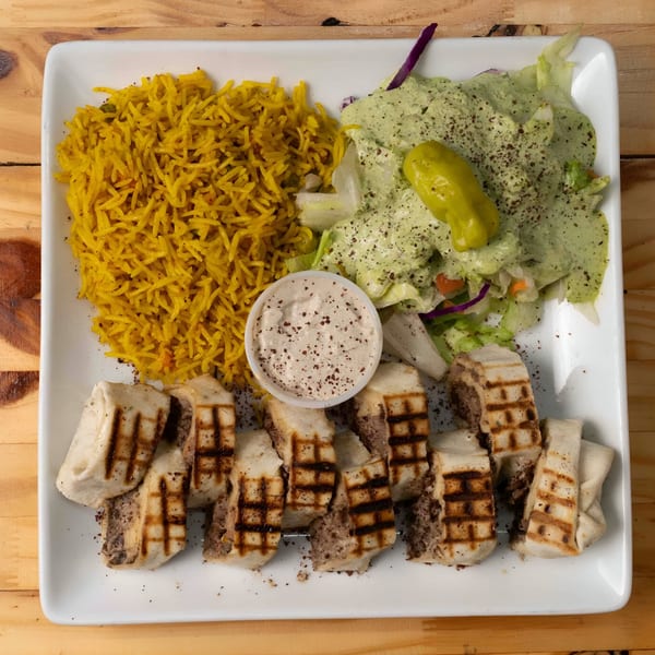 Hala Cafe's Mediterranean plate with yellow rice, salad with green dressing, and grilled meat wraps.