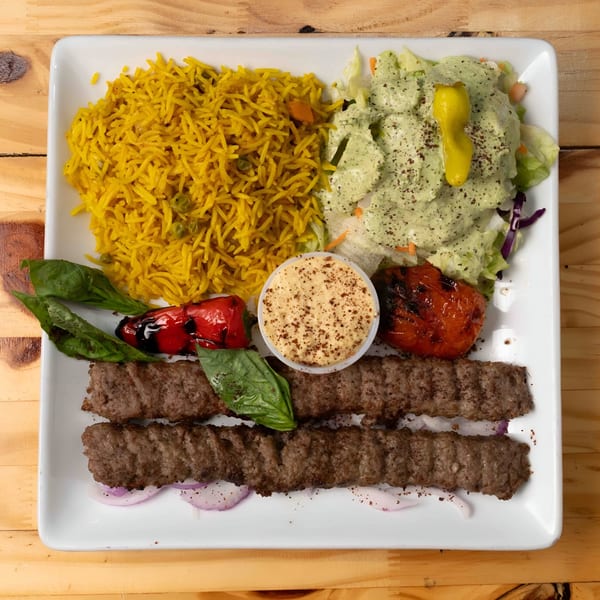 Hala Cafe's Mediterranean dish with two kebabs, yellow rice, salad, grilled vegetables, and dipping sauce.