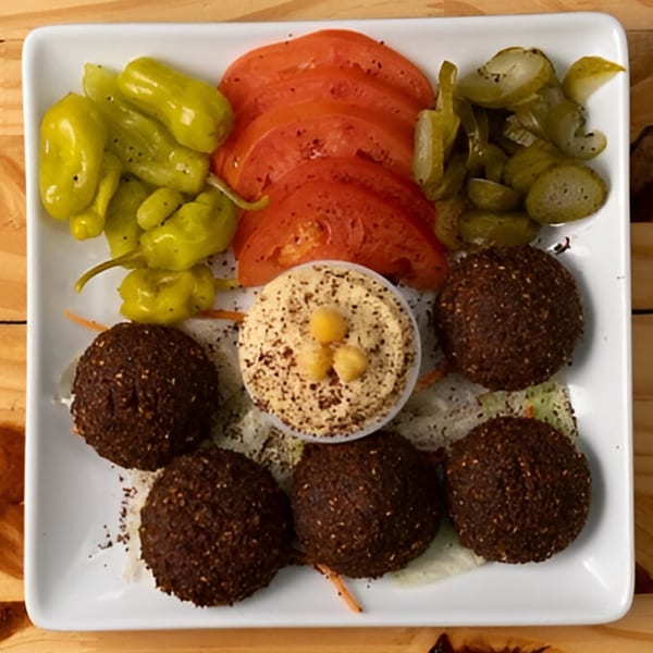 Hala Cafe's falafel platter with hummus, sliced tomatoes, pickled cucumbers, and green peppers.