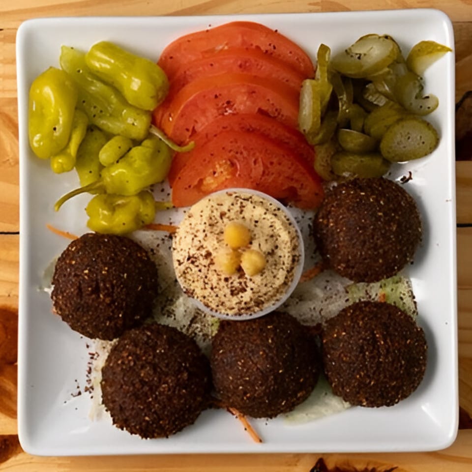 Hala Cafe's falafel platter with hummus, sliced tomatoes, pickled cucumbers, and green peppers.